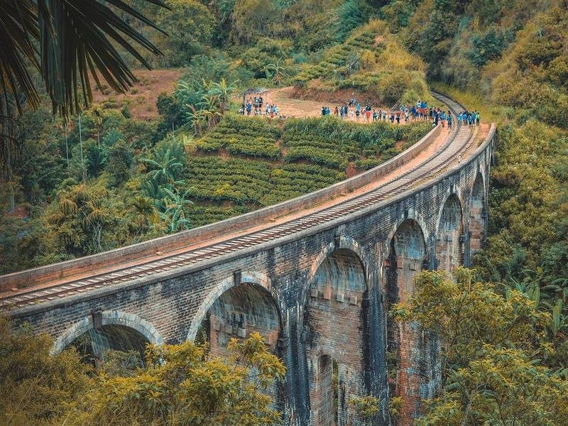 The Nine Arch Bridge near Ella curving through tea and forest, with walkers on the line